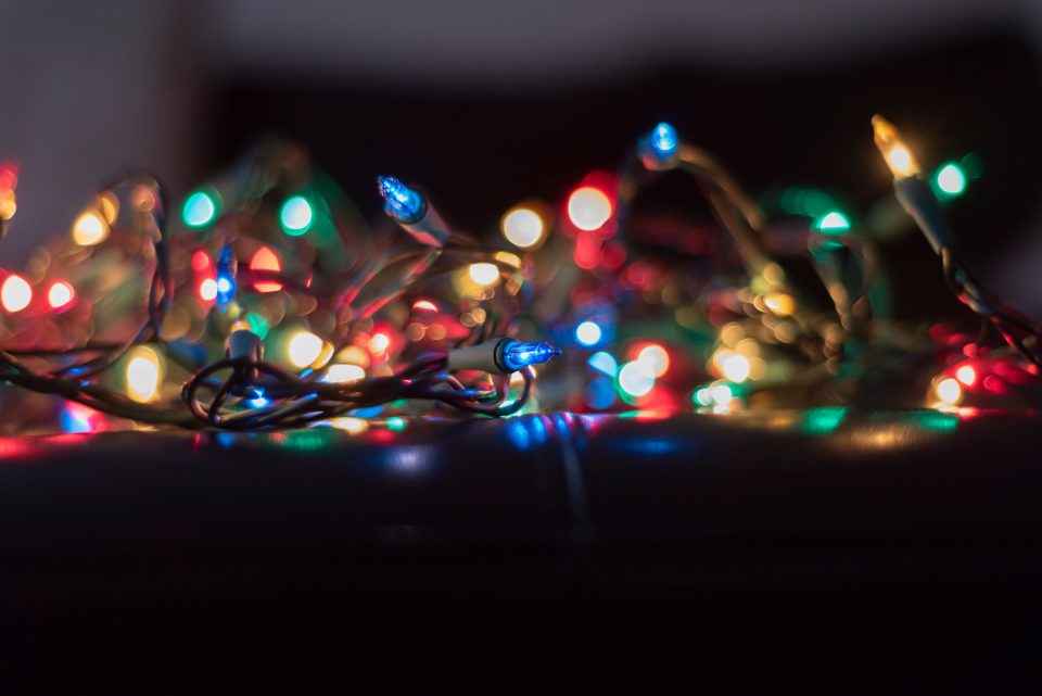 A detailed close-up shot of a tangled bundle of illuminated holiday lights featuring blue, red, green, and warm gold bulbs against a dark background with blurred bokeh lights.